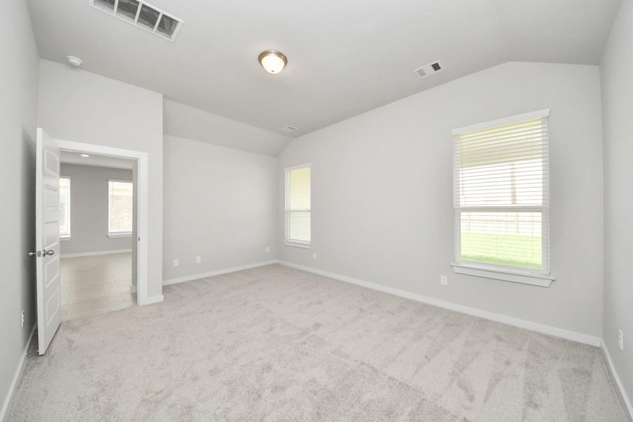 Escape and relax in the exquisite primary suite, a haven to unwind after a long day. The spacious room, located on first floor, boasts plush carpeting, soothing paint tones, high ceilings, and expansive windows adorned with privacy blinds. Sample photo of completed home with similar floor plan. Actual colors and selections may vary.