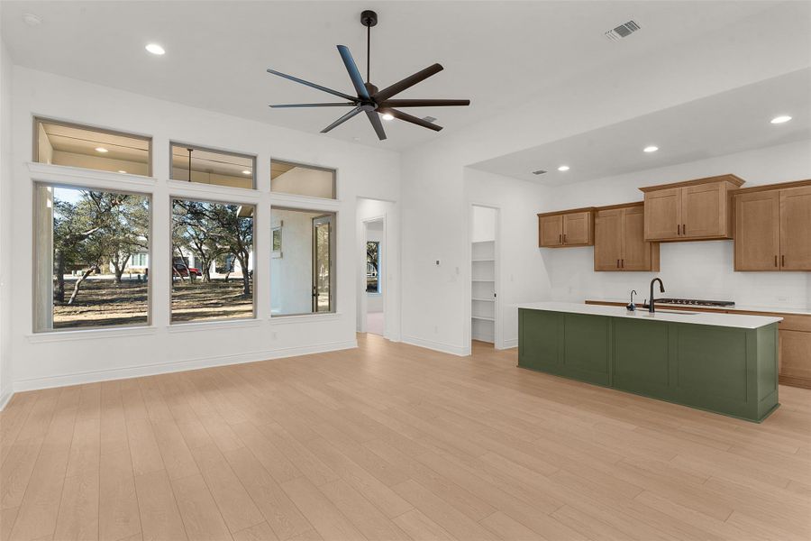 Dual tone kitchen with an island with sink, recessed lighting, ceiling fan, light wood-type flooring, and two tone color scheme