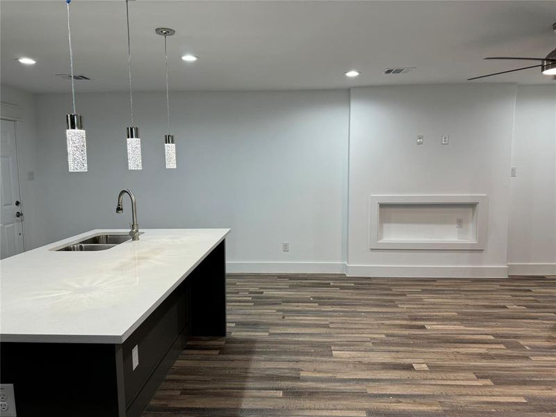 Kitchen with decorative light fixtures, dark hardwood / wood-style flooring, an island with sink, sink, and ceiling fan