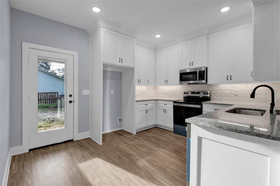 Kitchen with stainless steel appliances, white cabinets, light stone countertops, light wood finished floors, and decorative backsplash