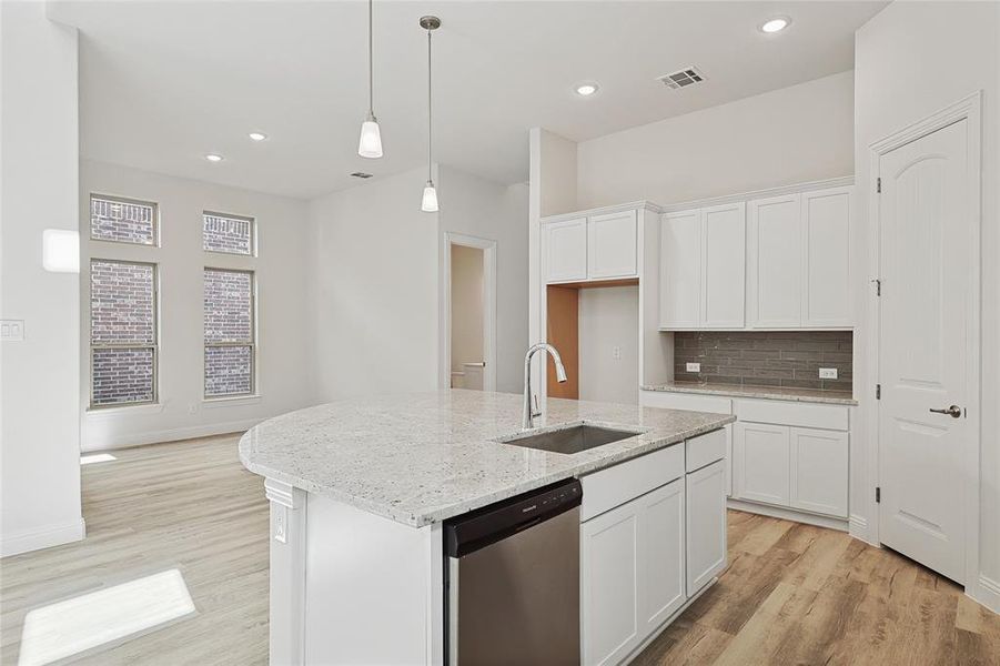 Kitchen with stainless steel dishwasher, white cabinets, sink, and an island with sink