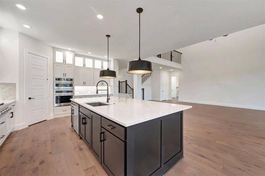 Kitchen with hanging light fixtures, light stone counters, dual tone cabinetry, light wood-style floors, and glass fronted cabinets
