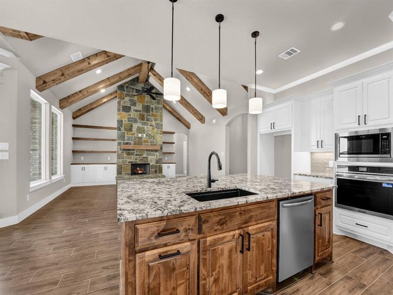 Kitchen featuring wood tiled floors, brown cabinetry, stainless steel appliances, an island with sink, and pendant lighting