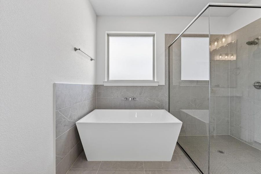 Freestanding soaking tub with wall-mounted faucet, complemented by a glass-enclosed walk-in shower featuring a built-in bench