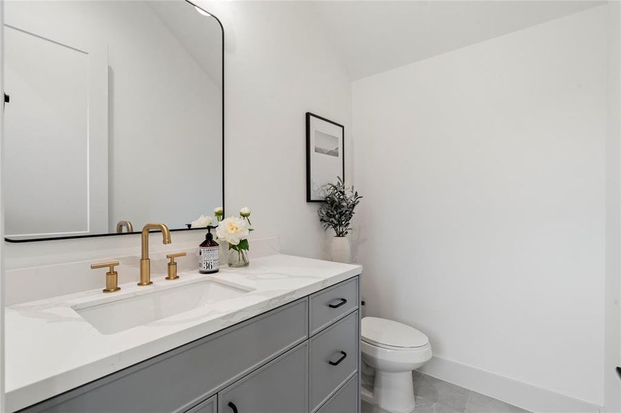 The half bathroom includes a vanity with quartz countertops, a contemporary sink, and a stylish gold faucet for a touch of elegance.