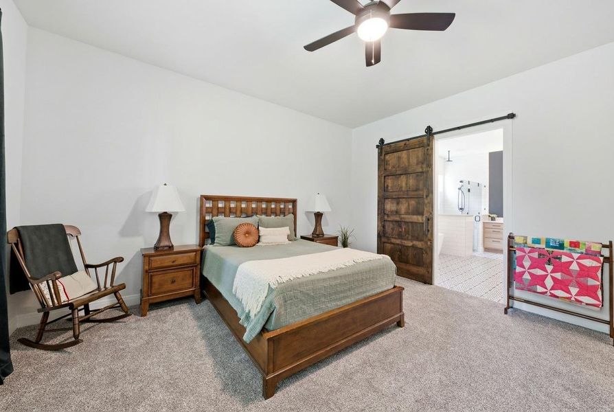 A quiet bedroom retreat with a barn door entrance to a primary bath, featuring cozy carpet underfoot. A quiet bedroom retreat with a barn door entrance to a primary bath, featuring cozy carpet underfoot.