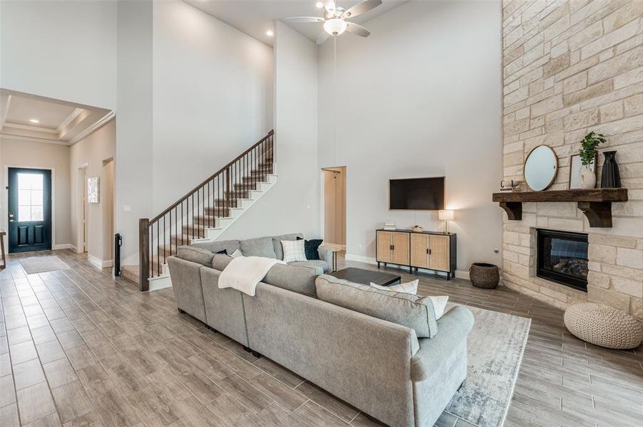 Living room featuring a fireplace, light wood-type flooring, ceiling fan, and a towering ceiling