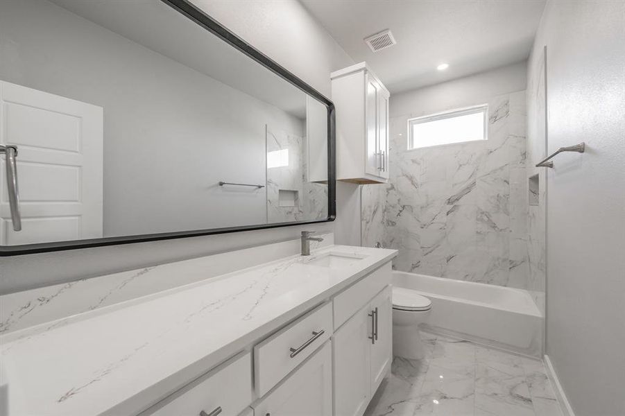 Full bathroom featuring vanity, tiled shower / bath combo, and toilet