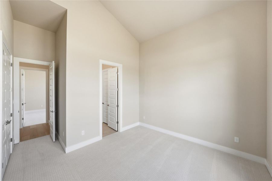 Unfurnished bedroom with vaulted ceiling and light colored carpet