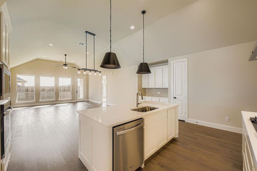 Kitchen with vaulted ceiling, dishwasher, white cabinetry, a kitchen island with sink, and ceiling fan Kitchen with vaulted ceiling, dishwasher, white cabinetry, a kitchen island with sink, and ceiling fan