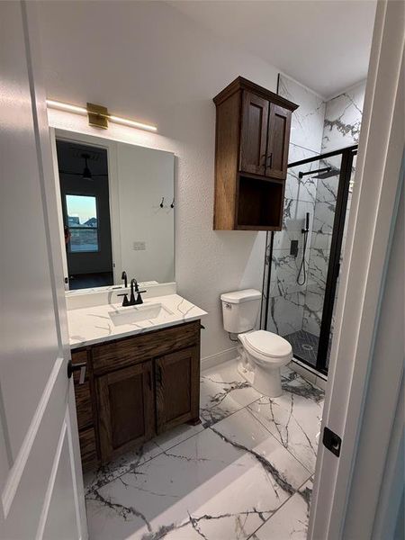 Bathroom featuring a marble finish shower, vanity, light marble finish floors, and a textured wall Bathroom featuring a marble finish shower, vanity, light marble finish floors, and a textured wall