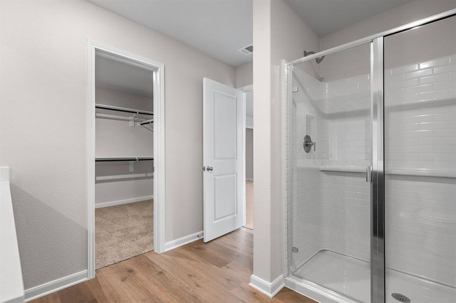 Bathroom featuring a stall shower, light wood-style floors, and a spacious closet Bathroom featuring a stall shower, light wood-style floors, and a spacious closet