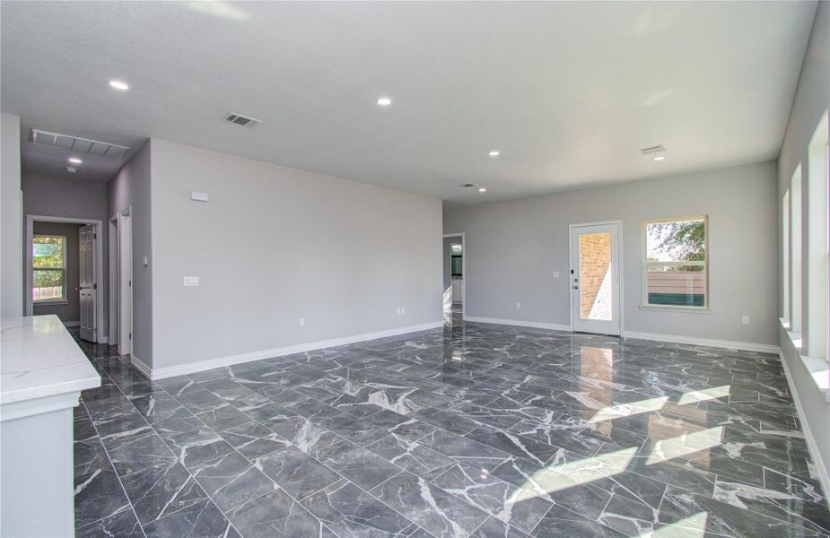 This spacious living area features sleek gray marble flooring, ample natural light from multiple windows, and recessed lighting. The open layout is ideal for versatile furnishing, with a modern, neutral color scheme that complements any decor.
