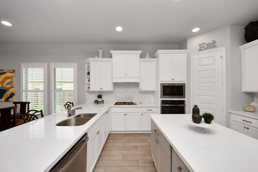 This photo showcases a modern kitchen with sleek white cabinetry, a large island with a sink, and stainless steel appliances. It features bright, natural lighting from windows with shutters, and has a clean, contemporary design.