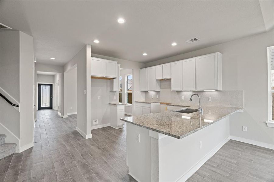 Culinary haven, featuring granite countertops, a tile backsplash, stainless steel appliances (to be installed), and 42” upper cabinets. Sample photo, actual color and selections may vary.