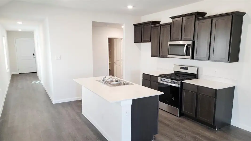 Kitchen with stainless steel appliances, dark wood-style flooring, an island with sink, recessed lighting, and dark brown cabinetry Kitchen with stainless steel appliances, dark wood-style flooring, an island with sink, recessed lighting, and dark brown cabinetry