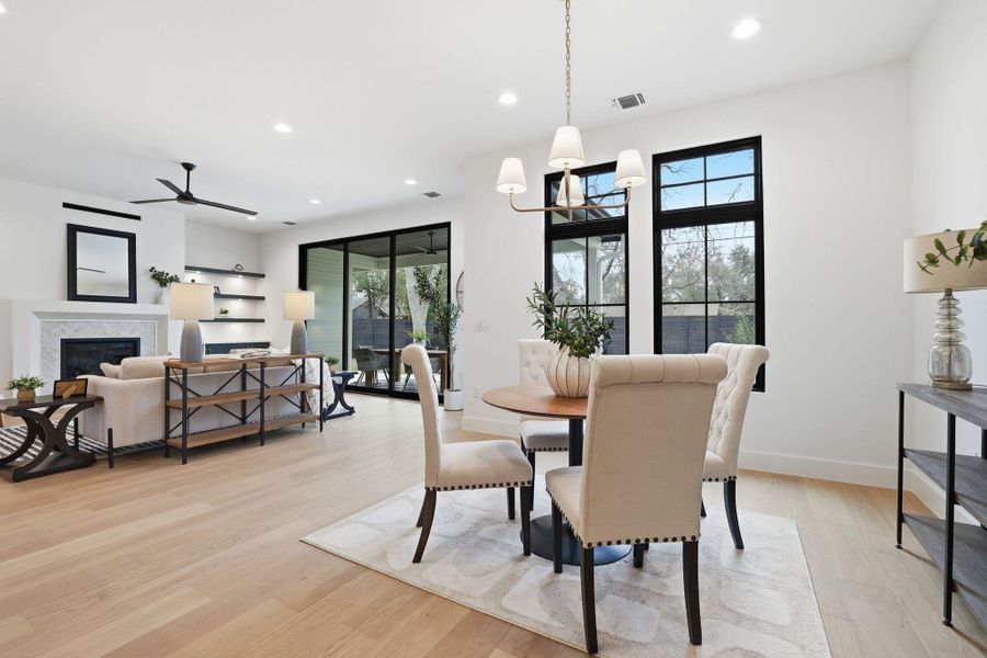 Dining area featuring a ceiling fan, a high end fireplace, light wood-style floors, and a chandelier