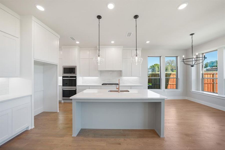 Kitchen with decorative light fixtures, white cabinets, light stone counters, light wood-style flooring, and a kitchen island with sink Kitchen with decorative light fixtures, white cabinets, light stone counters, light wood-style flooring, and a kitchen island with sink