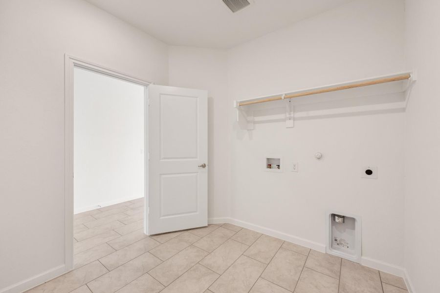 Empty laundry room with tile floor, wall-mounted shelf, washer hookups, and open white door