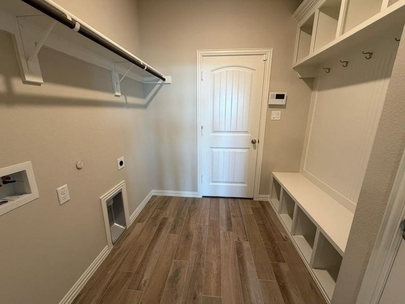 Dedicated laundry area featuring wood-finish flooring, built-in shelving, a garment rod, and a built-in mudroom bench with cubbies and coat hooks