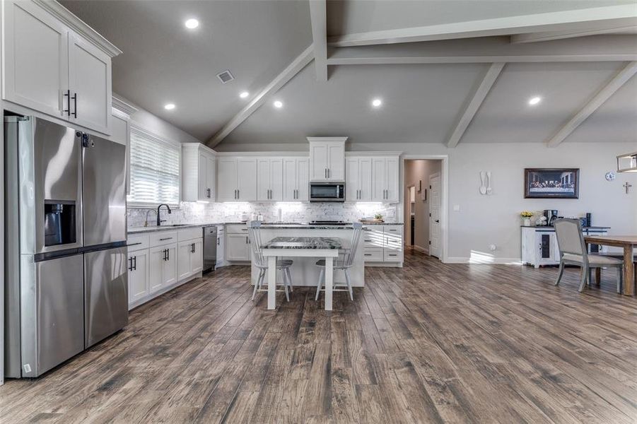 Kitchen featuring stainless steel appliances, a center island, backsplash, white cabinetry, and dark wood finished floors