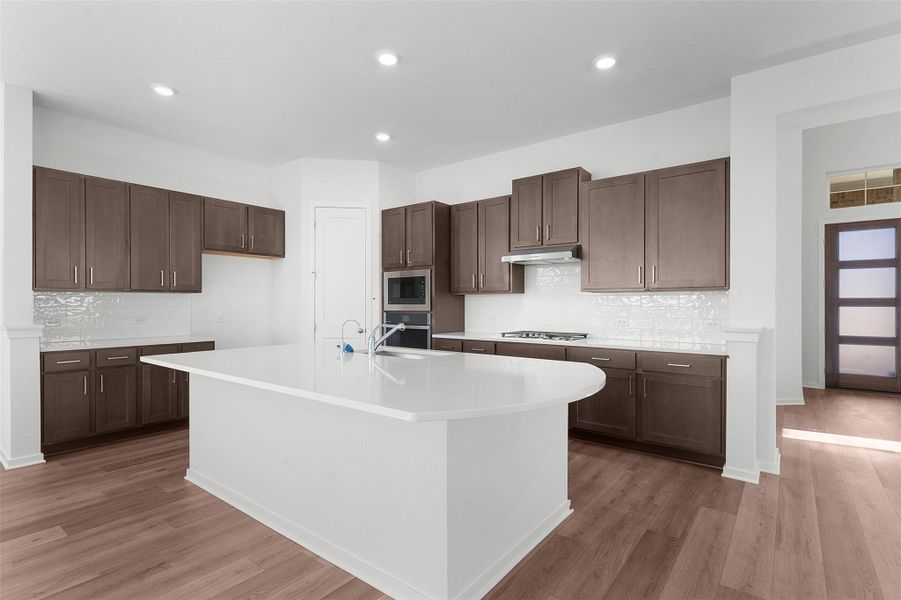 Kitchen with decorative backsplash, dark brown cabinetry, light wood-style flooring, a kitchen island with sink, and recessed lighting