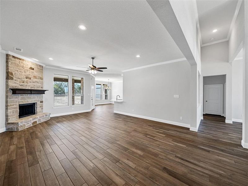 Prior listing photo. Property remains accurate - Unfurnished living room with a stone fireplace, ornamental molding, dark wood-type flooring, ceiling fan, and a chandelier