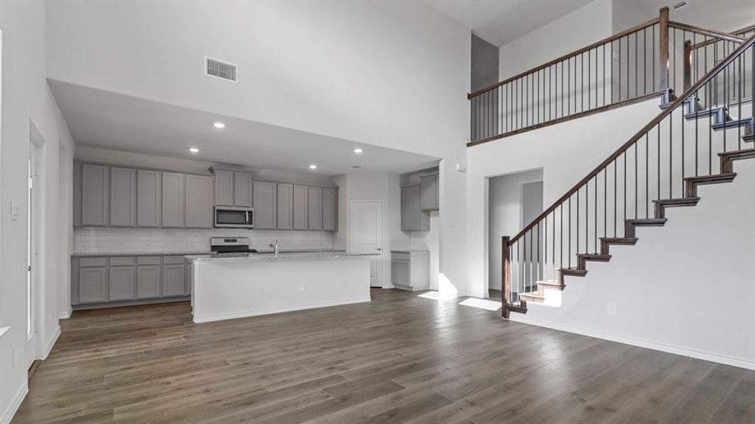 Kitchen featuring gray cabinets, a kitchen island with sink, stainless steel appliances, dark wood-style floors, and decorative backsplash