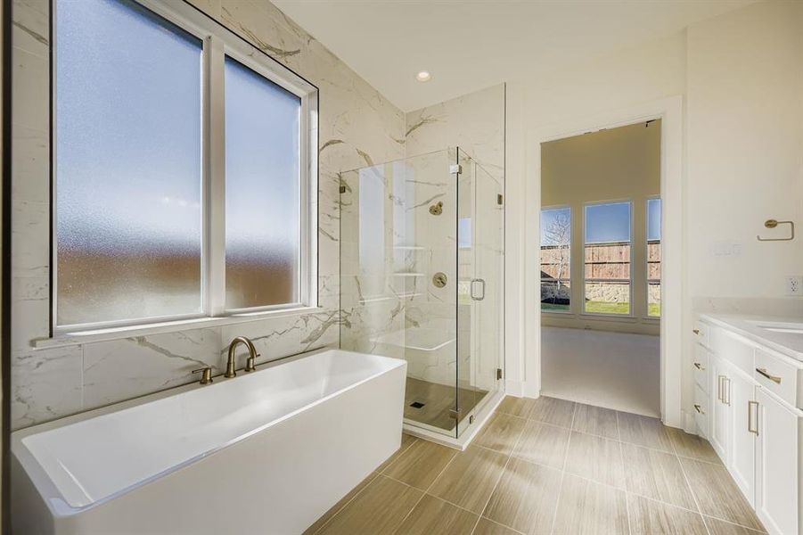 Full bath featuring a soaking tub, vanity, and a marble finish shower