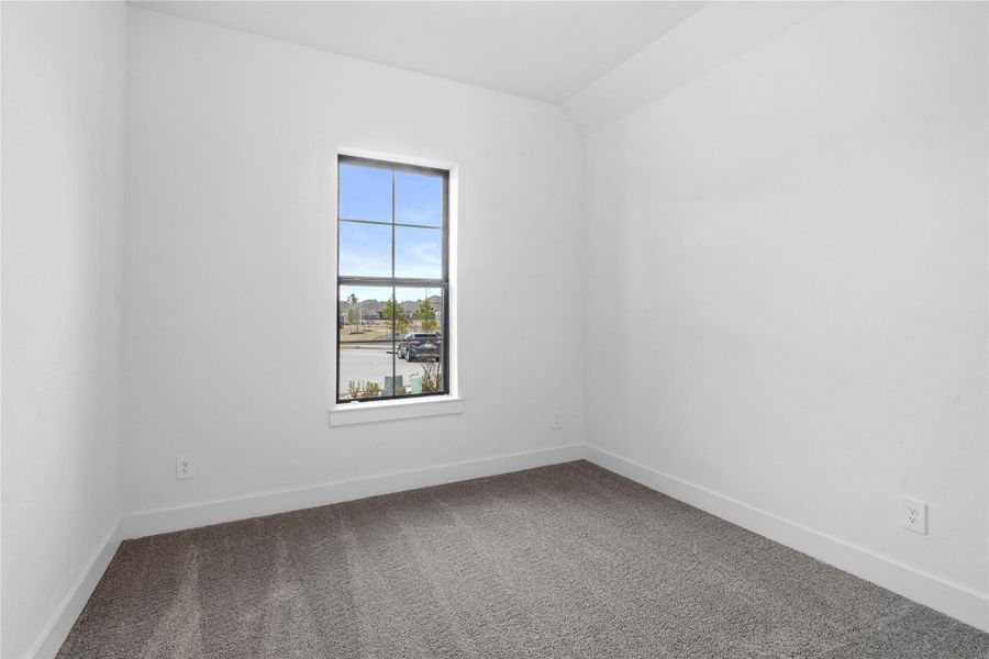Tucked peacefully in the front of the home is this secondary bedroom featuring neutral toned walls, sloped ceiling, large window, plush carpet flooring, and a walk-in closet.