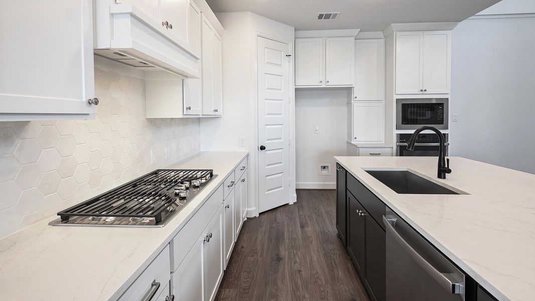Kitchen with dark wood-style floors, light stone counters, white cabinetry, stainless steel appliances, and under cabinet range hood