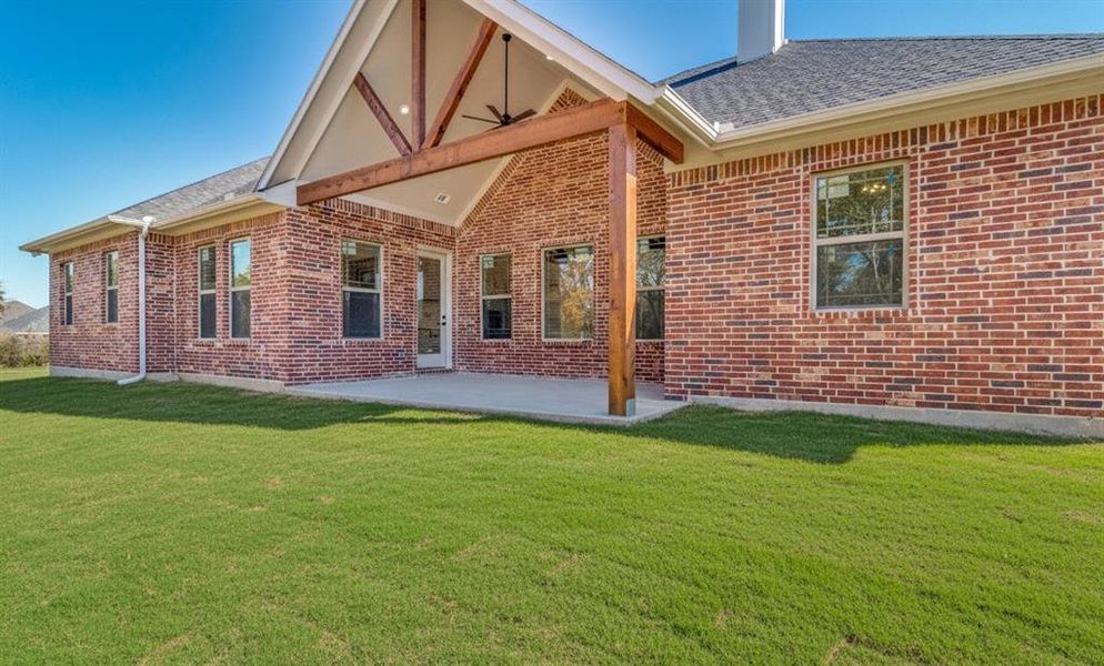 Rear view of property with a patio area, brick siding, a shingled roof, and a yard