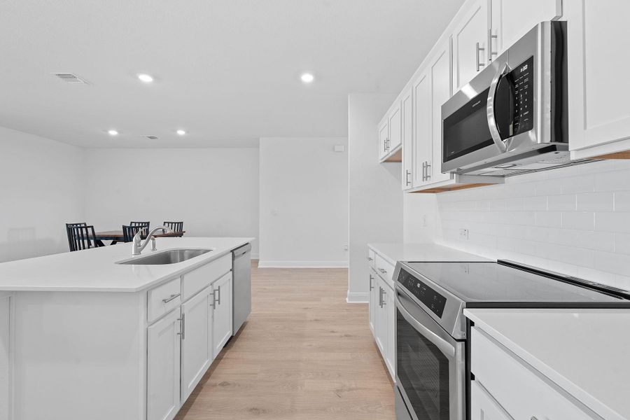Kitchen with stainless steel appliances, white cabinetry, light wood-type flooring, recessed lighting, and an island with sink Kitchen with stainless steel appliances, white cabinetry, light wood-type flooring, recessed lighting, and an island with sink