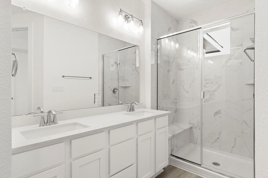 Full bath with double vanity and a marble finish shower