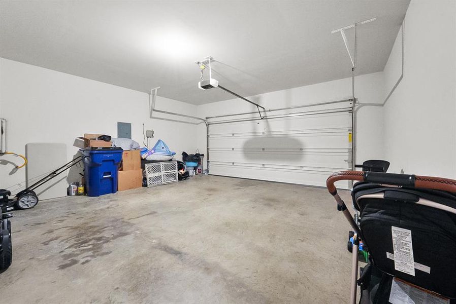 Spacious garage with a sectional overhead door, exposed garage door opener, and a light-colored concrete floor