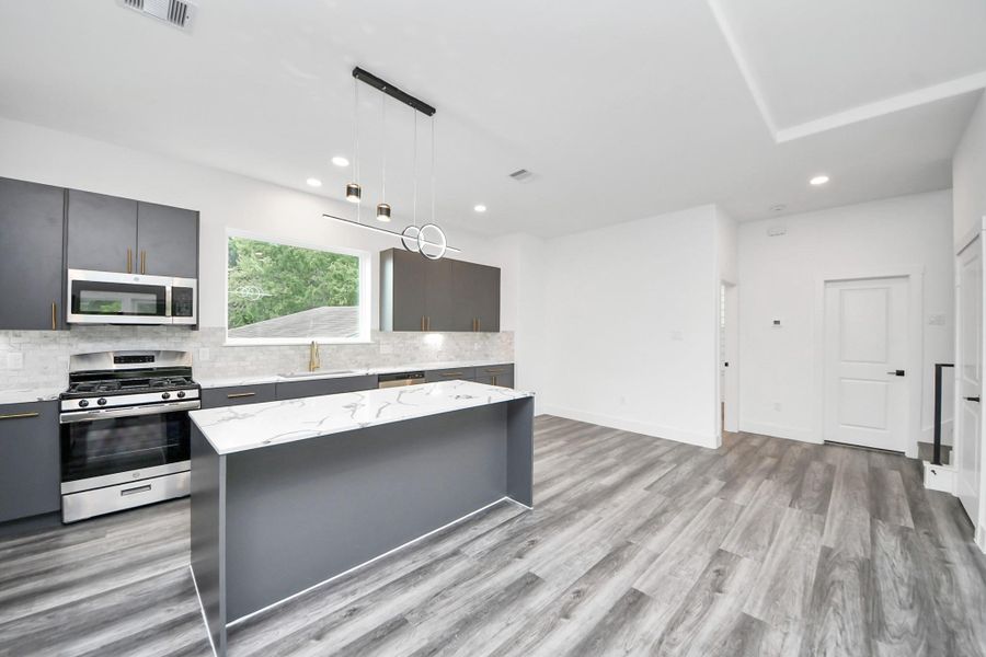 Modern kitchen with sleek dark cabinetry and stainless steel appliances. Features a large island with a marble countertop and contemporary pendant lighting. Bright and airy with light wood flooring and ample natural light from a large window. Modern kitchen with sleek dark cabinetry and stainless steel appliances. Features a large island with a marble countertop and contemporary pendant lighting. Bright and airy with light wood flooring and ample natural light from a large window.