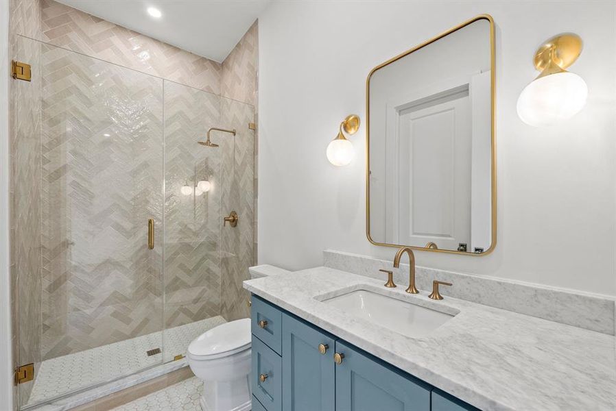 Bathroom featuring a shower with herringbone tile, a blue vanity with a white countertop, and a gold-framed mirror