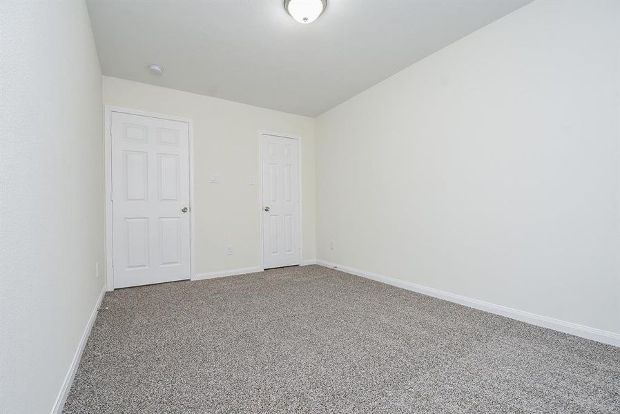 Empty room with two closed white doors, textured carpet, and white walls with one ceiling light fixture.