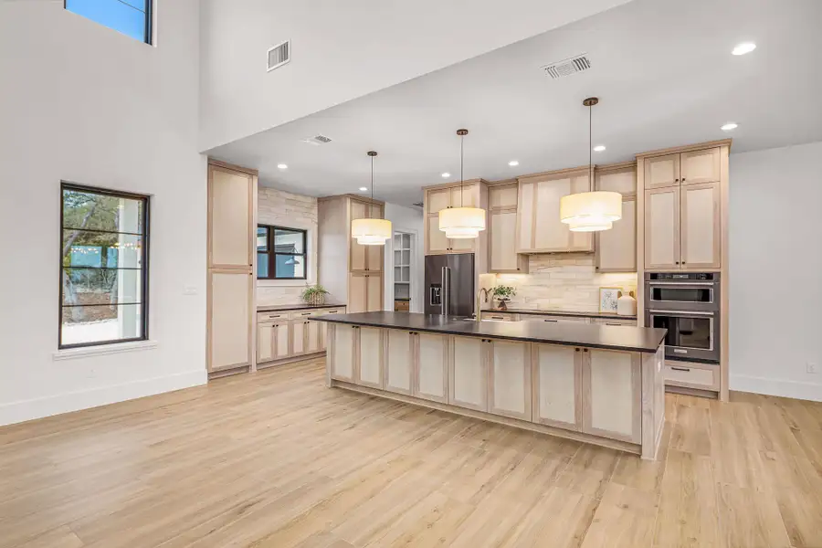 Kitchen with dark countertops, light brown cabinetry, high end fridge, and decorative light fixtures