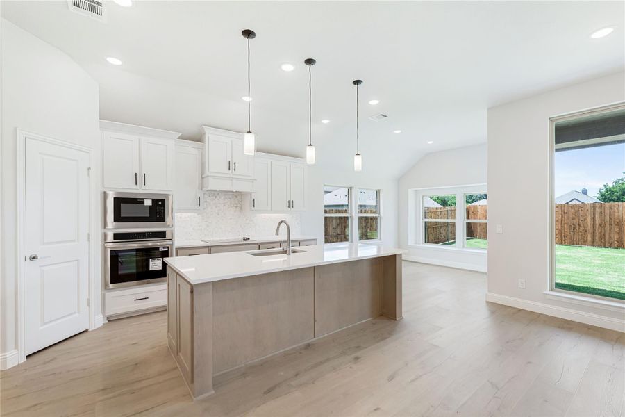 Open kitchen with large island, white cabinets, stainless steel appliances, pendant lights, and light wood floors