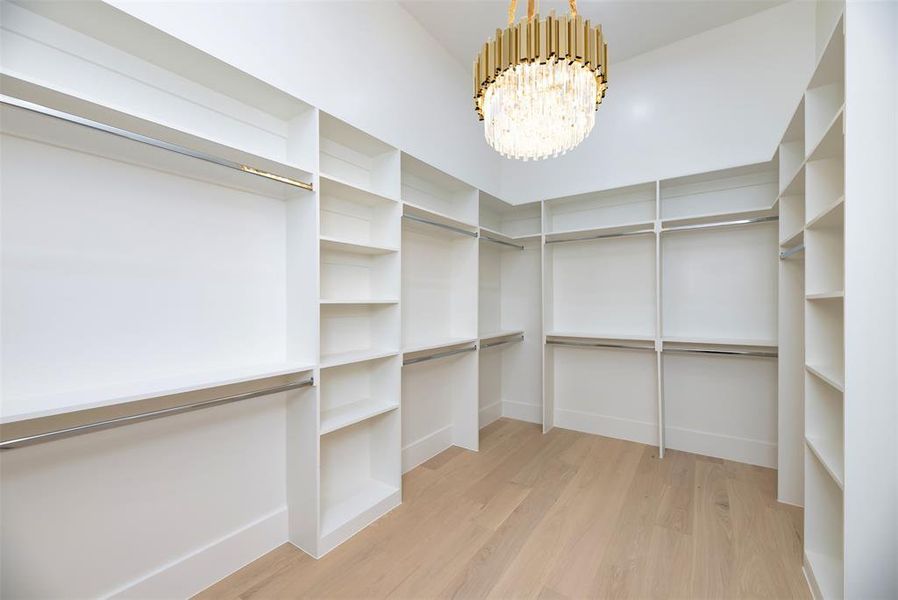 Walk in closet featuring a chandelier and light wood-style flooring Walk in closet featuring a chandelier and light wood-style flooring