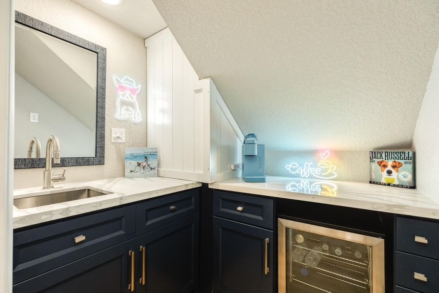 Convenient beverage station includes custom cabinetry, quartz countertops, a built-in beverage refrigerator, and additional storage for entertaining essentials.