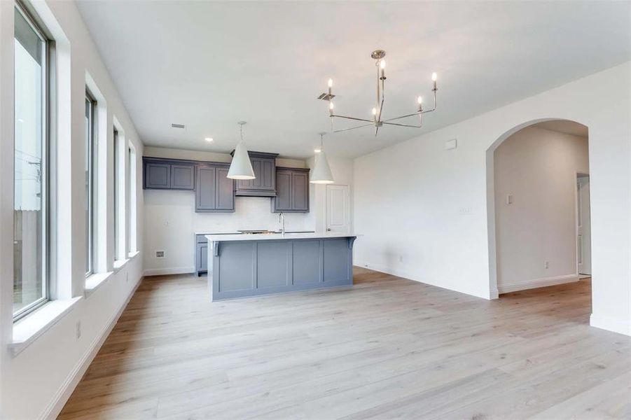Kitchen featuring light wood-type flooring, a center island with sink, arched walkways, baseboards, and a chandelier