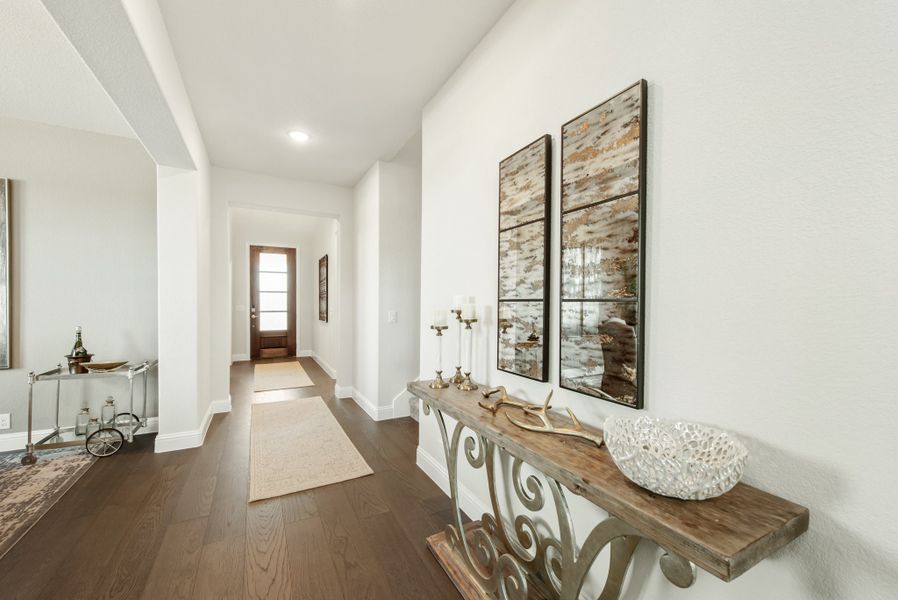 Hallway with dark hardwood floors, wood console table, decorative mirrors, and a glass front door at the end.