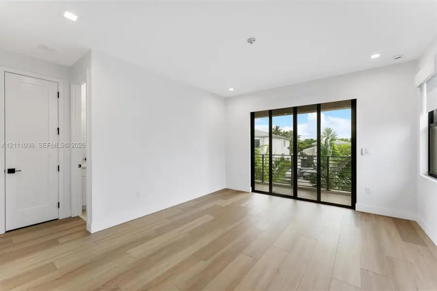 Wood-finish flooring, recessed lighting, multi-panel sliding glass doors with black frames, and a private balcony