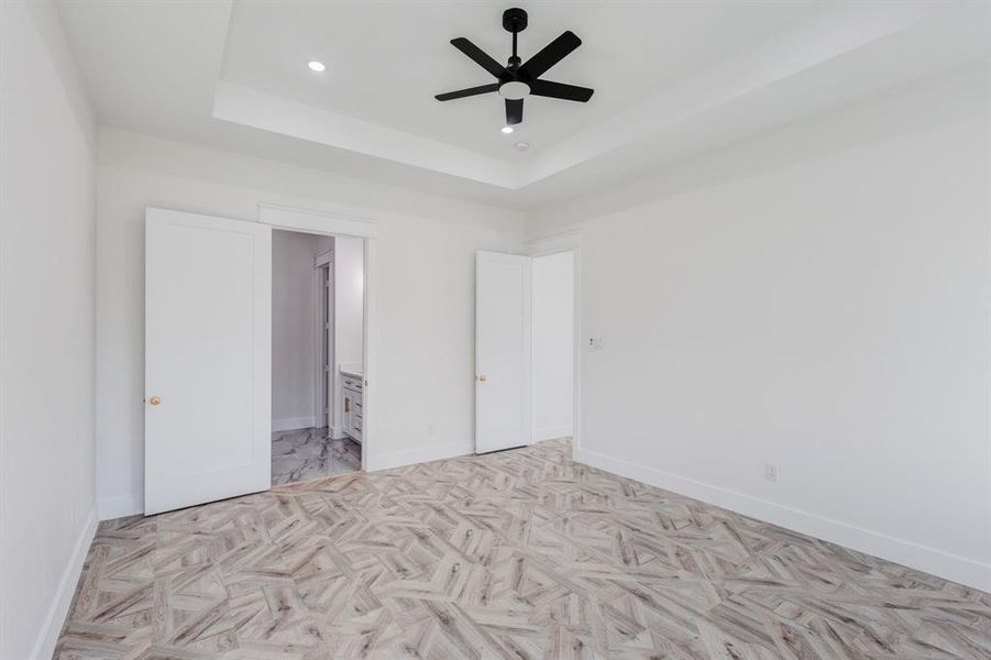 Unfurnished bedroom with ensuite bathroom, a raised ceiling, and ceiling fan