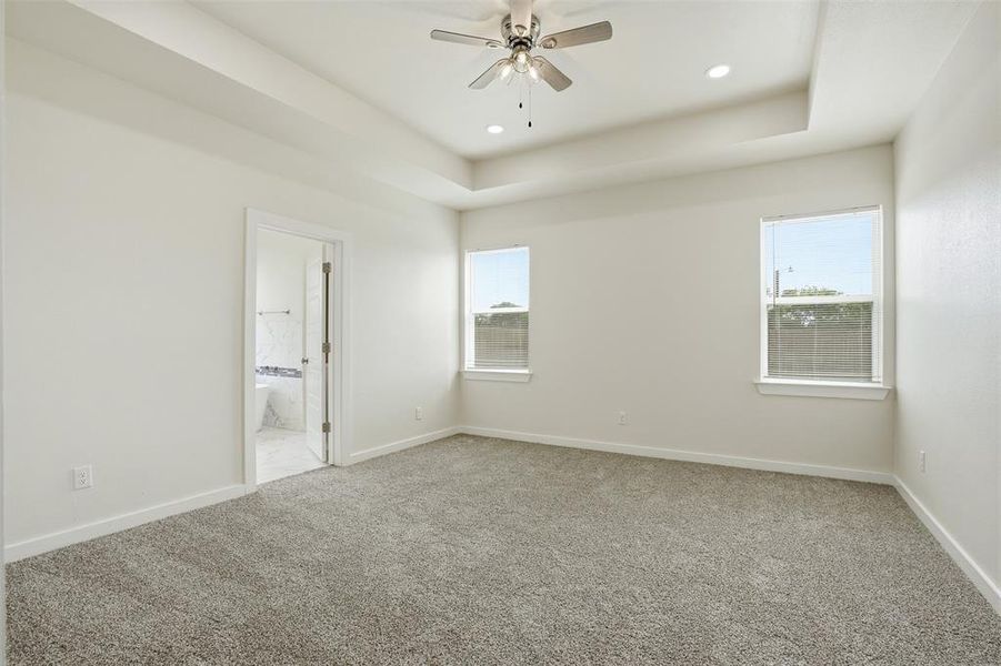 Spacious room featuring tray ceilings with recessed lighting and a ceiling fan