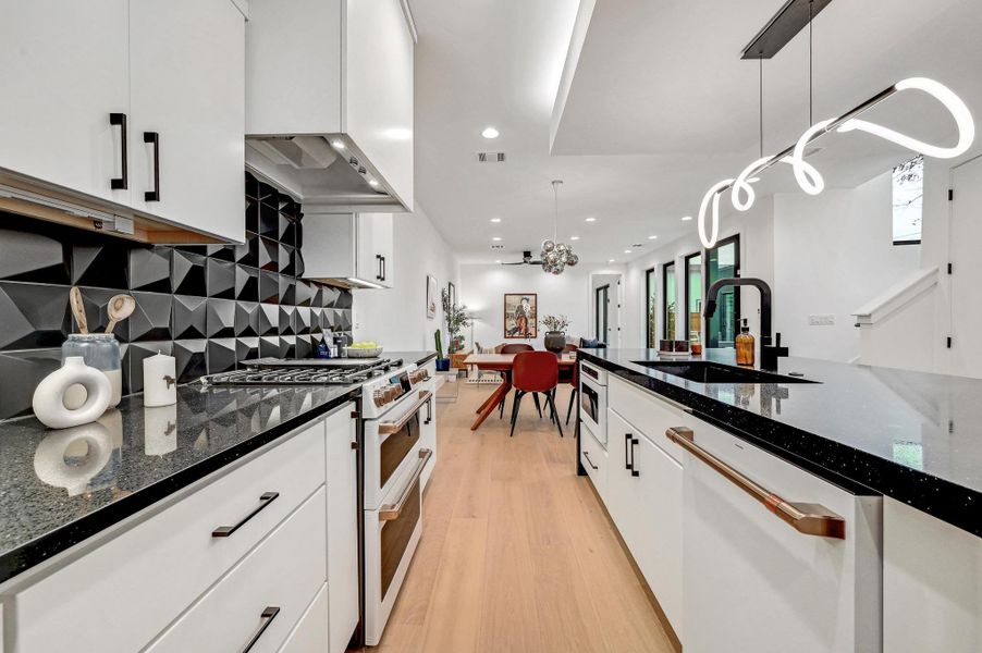 Kitchen with dark stone countertops, white cabinets, decorative light fixtures, light wood-style floors, and white appliances