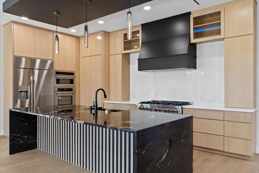 Kitchen featuring wood cabinetry, glass insert cabinets, appliances with stainless steel finishes, premium range hood, and dark stone countertops Kitchen featuring wood cabinetry, glass insert cabinets, appliances with stainless steel finishes, premium range hood, and dark stone countertops