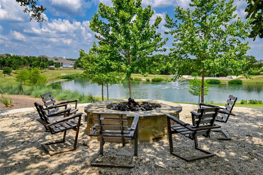 Outdoor fire pit area with seating, overlooking a serene body of water with a fountain